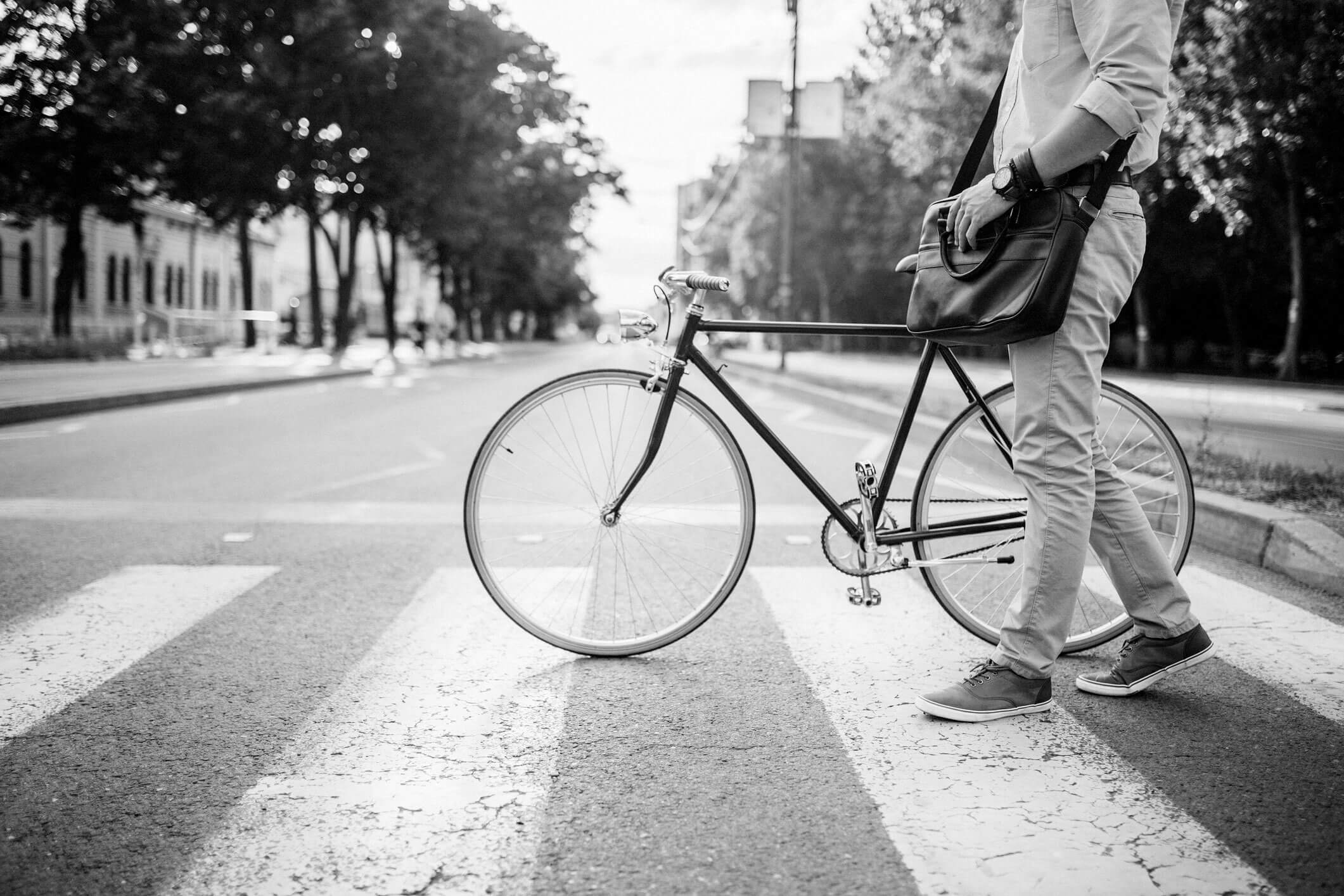 A man walks his bicycle along a crosswalk on a city street.