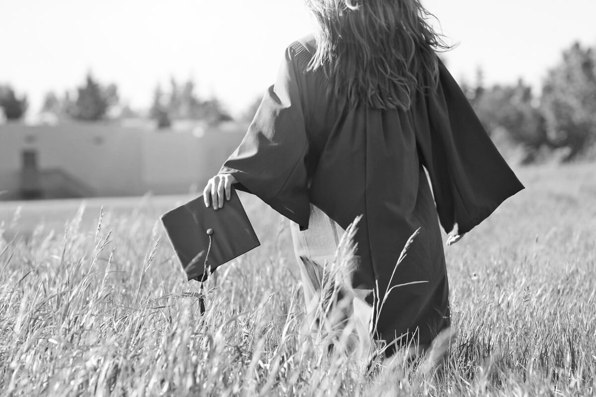 Young female graduate running through the tall grass.